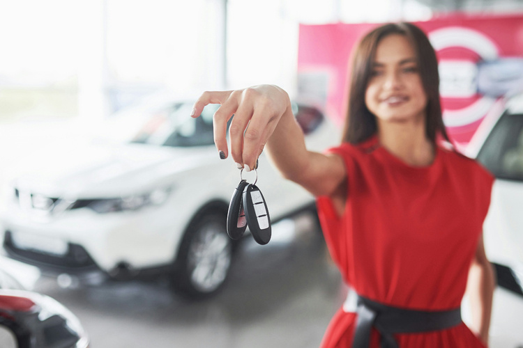 Mujer en concesionario mostrando las llaves de un vehículo nuevo - Publicidad automotriz